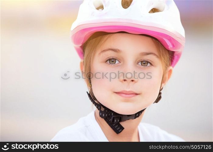 Closeup portrait of cute little biker girl wearing pretty pink and white helmet, having fun outdoors, with pleasure spending time in summer camp