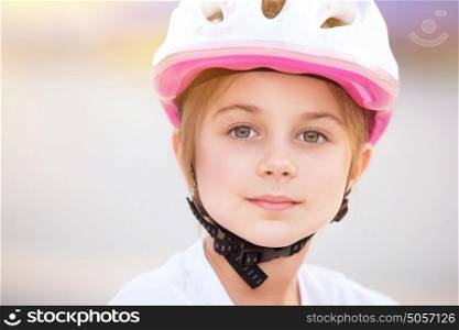 Closeup portrait of cute little biker girl wearing pretty pink and white helmet, having fun outdoors, with pleasure spending time in summer camp
