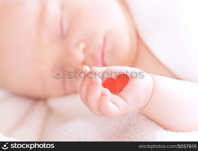 Closeup portrait of cute newborn baby sleeping, holding in hand little red heart, innocent child, soft focus, hope and help concept
