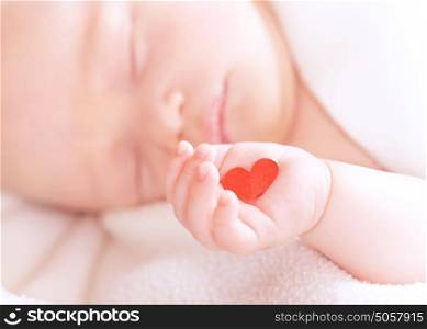 Closeup portrait of cute newborn baby sleeping, holding in hand little red heart, innocent child, soft focus, hope and help concept