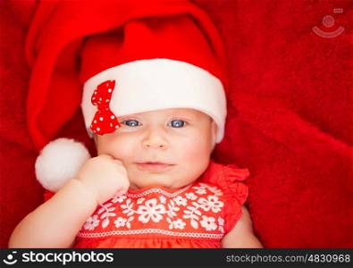 Closeup portrait of cute newborn girl wearing Santa hat, lying down on red background, Christmas holiday, festive baby fashion concept&#xA;