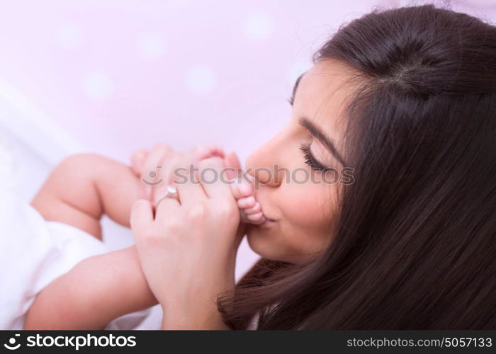 Closeup portrait of cute peaceful mother kissing feet of her little baby, happy young family, loving and protecting child concept