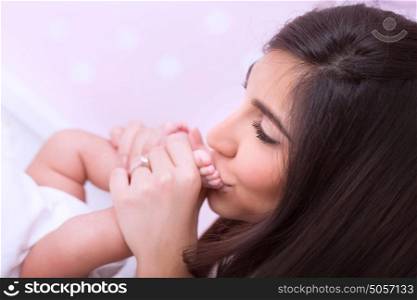 Closeup portrait of cute peaceful mother kissing feet of her little baby, happy young family, loving and protecting child concept