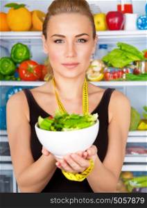 Closeup portrait of cute serious woman with measure tape and fresh vegetables salad, refrigerator full of vegetables, sportive trainer, organic food, health and beauty care concept