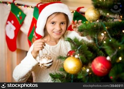 Closeup portrait of cute smiling girl decorating Christmas tree with golden balls