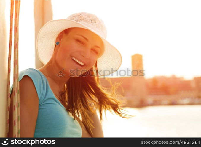 Closeup portrait of cute smiling woman on orange sunset background, wearing white stylish hat, glamorous lifestyle, wonderful trip on the yacht