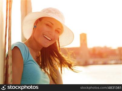 Closeup portrait of cute smiling woman on orange sunset background, wearing white stylish hat, glamorous lifestyle, wonderful trip on the yacht