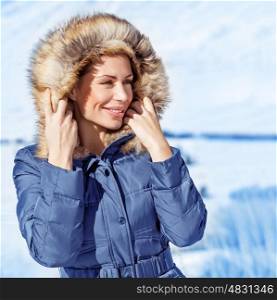 Closeup portrait of cute woman wearing warm coat with hood with fur, having fun in winter park, wintertime fashionable style, vacation concept