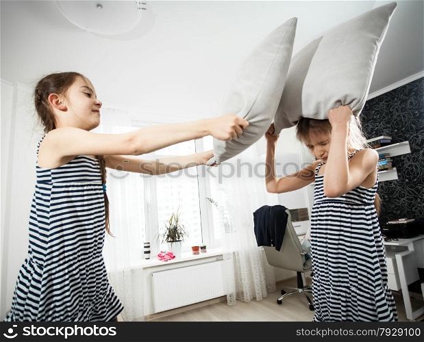 Closeup portrait of girl hitting sister with pillow during fight