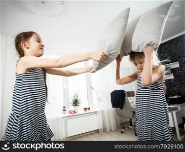 Closeup portrait of girl hitting sister with pillow during fight