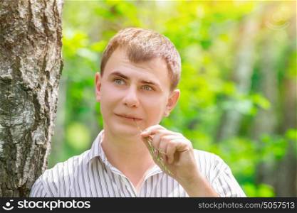 Closeup portrait of handsome dreamy guy in fresh spring park, spending time outdoors in bright sunny day, peace and relaxation concept