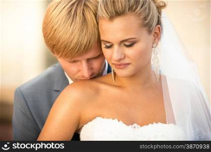 Closeup portrait of handsome groom kissing blonde bride in shoulder