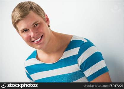 Closeup portrait of handsome young man leaning on white wall and smiling