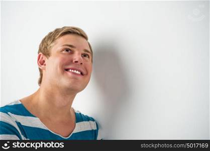 Closeup portrait of handsome young man leaning on white wall, daydreaming and smiling