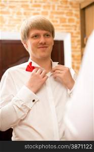 Closeup portrait of handsome young man putting on red bow tie