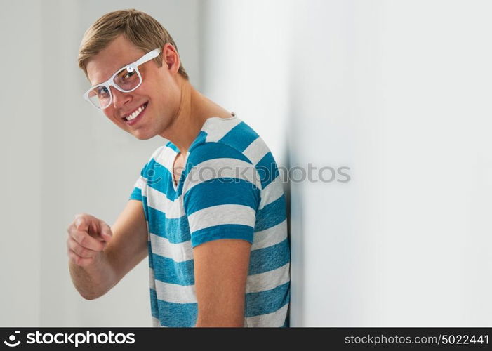 Closeup portrait of handsome young man wearing glasses leaning on white wall and smiling