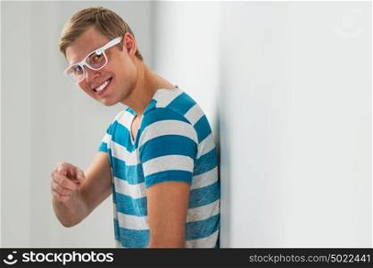 Closeup portrait of handsome young man wearing glasses leaning on white wall and smiling