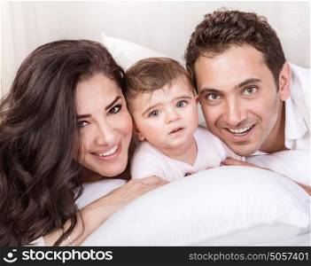 Closeup portrait of happy arabic family, beautiful mother and handsome father with baby daughter lying down and having fun in bedroom, love and unity concept