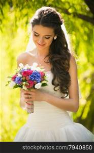 Closeup portrait of happy brunette bride looking at wedding bouquet at park