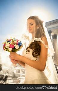 Closeup portrait of happy brunette bride posing with wedding bouquet at sunny day
