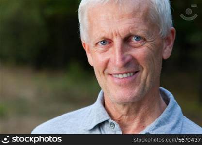 Closeup portrait of happy face of grey-haired old man. Outdoor. In the park. Blue jeans. Grey t-shirt.