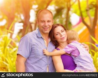 Closeup portrait of happy family in the park, mother carry little baby boy, parents with cute child enjoying warm sunny day, love and happiness concept