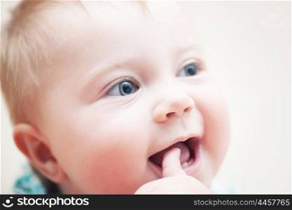 Closeup portrait of happy funny baby with finger in the mouth, adorable sweet child with beautiful grey eyes, healthy childhood