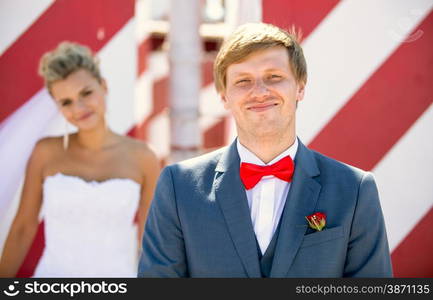 Closeup portrait of happy smiling groom posing on street against out of focus bride