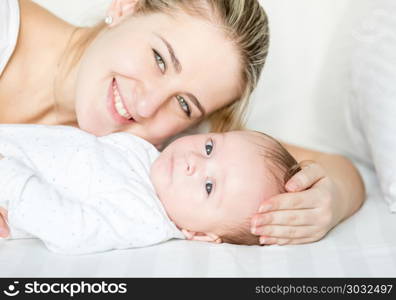 Closeup portrait of happy smiling mother and baby lying on bed and looking in camera. Portrait of happy smiling mother and baby lying on bed and looking in camera