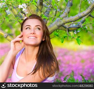 Closeup portrait of happy woman in blooming garden, having fun outdoors, sitting down on pink floral meadow, spring time concept