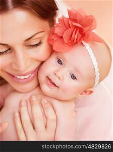 Closeup portrait of happy young mother hugging sweet little newborn daughter, cute baby girl wearing red floral head decoration, love concept