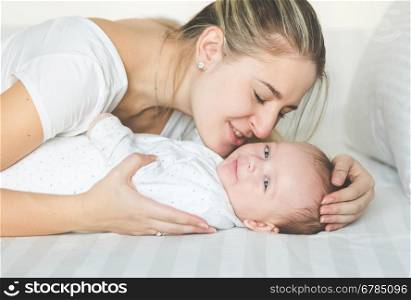 Closeup portrait of happy young mother kissing her baby boy on bed