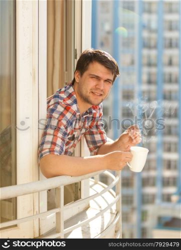 Closeup portrait of hipster guy drinking coffee on balcony