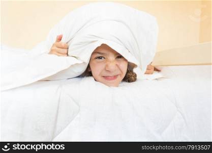 Closeup portrait of little angry girl lying in bed with pillow on head