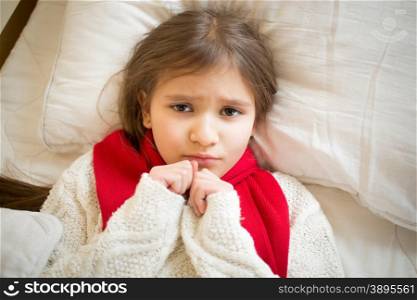 Closeup portrait of little sad girl with flu lying in bed