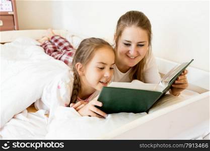 Closeup portrait of mother lying with daughter on bed and reading book