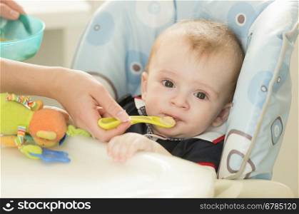 Closeup portrait of mothers hand giving food in spoon to her baby boy