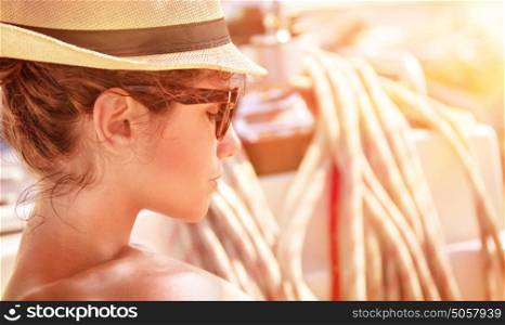 Closeup portrait of of cute female relaxing on the yacht in mild sunset light, side view of attractive woman wearing stylish hat and sunglasses, summer vacation concept