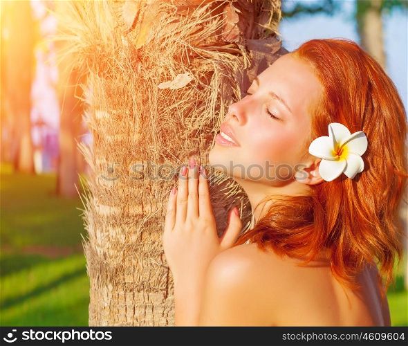 Closeup portrait of pretty redhead woman with frangipani flower in hair and closed eyes enjoying warm sun light, luxury tropical resort, summer time vacation and holidays
