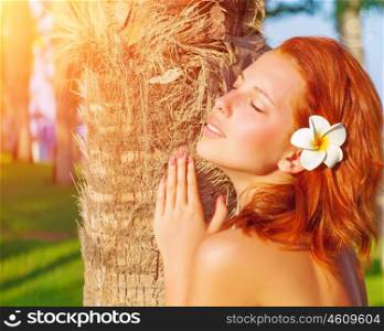 Closeup portrait of pretty redhead woman with frangipani flower in hair and closed eyes enjoying warm sun light, luxury tropical resort, summer time vacation and holidays