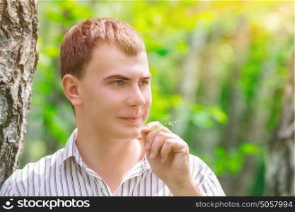Closeup portrait of romantic guy in the park, standing near birch tree with straw in the mouth, waiting for his girlfriend, enjoying beauty of spring nature