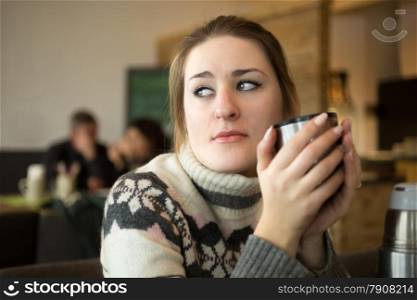 Closeup portrait of sad woman in sweater drinking coffee at cafe
