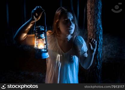 Closeup portrait of scared woman lost in forest lighting up the way with lantern