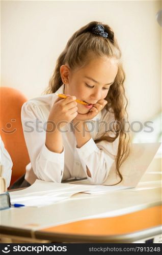 Closeup portrait of schoolgirl chewing pencil while doing homework