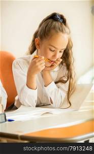 Closeup portrait of schoolgirl chewing pencil while doing homework