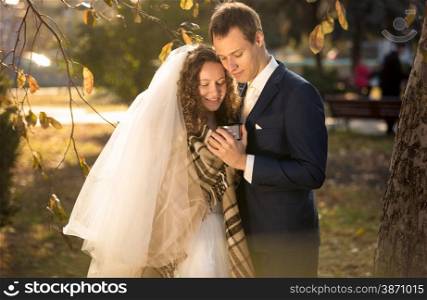 Closeup portrait of smiling bride and groom holding cup of tea at park