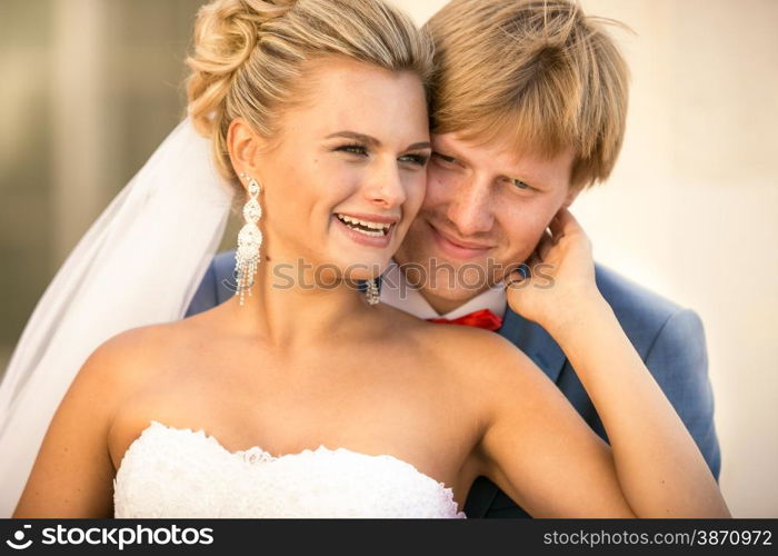 Closeup portrait of smiling bride and groom hugging on street at sunny day
