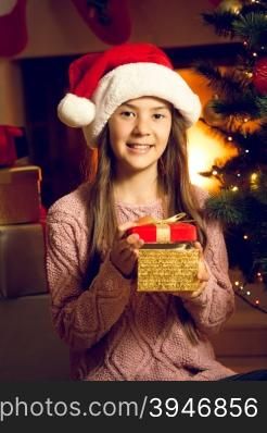 Closeup portrait of smiling girl in Santa cap holding red gift box