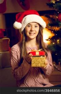 Closeup portrait of smiling girl in Santa cap holding red gift box