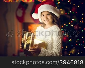Closeup portrait of smiling girl in Santa cap posing with glowing gift box